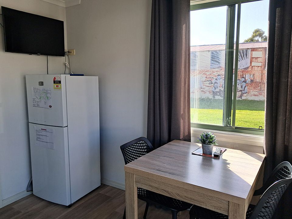Small dining area with a table, chairs, refrigerator, wall TV, and a large window overlooking greenery.