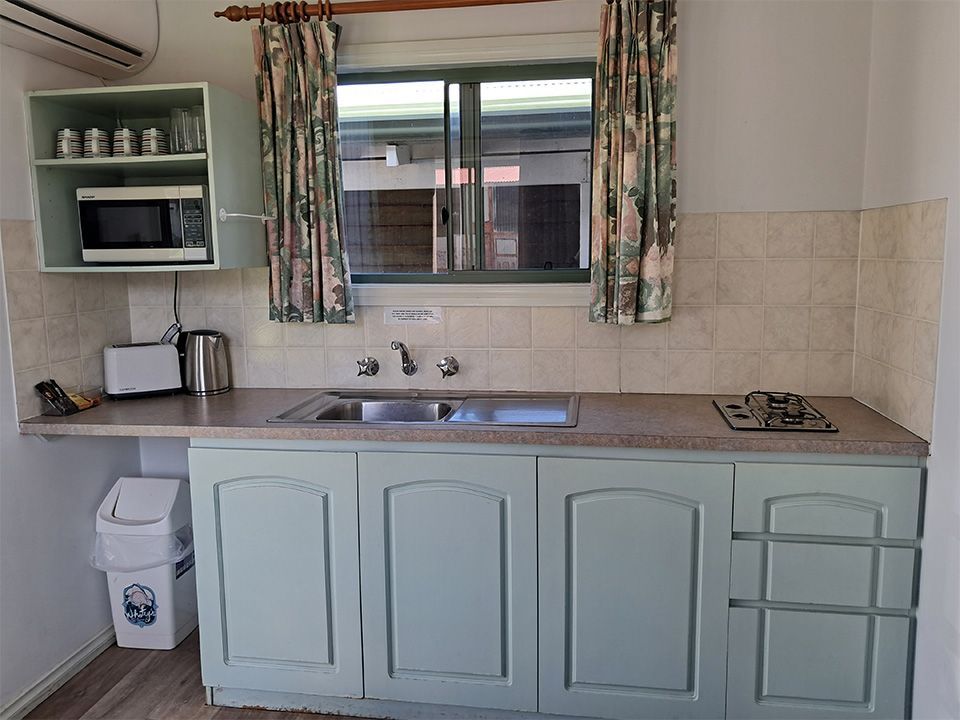 Compact kitchen with pale blue cabinets, sink under a window, and a stove on the right.