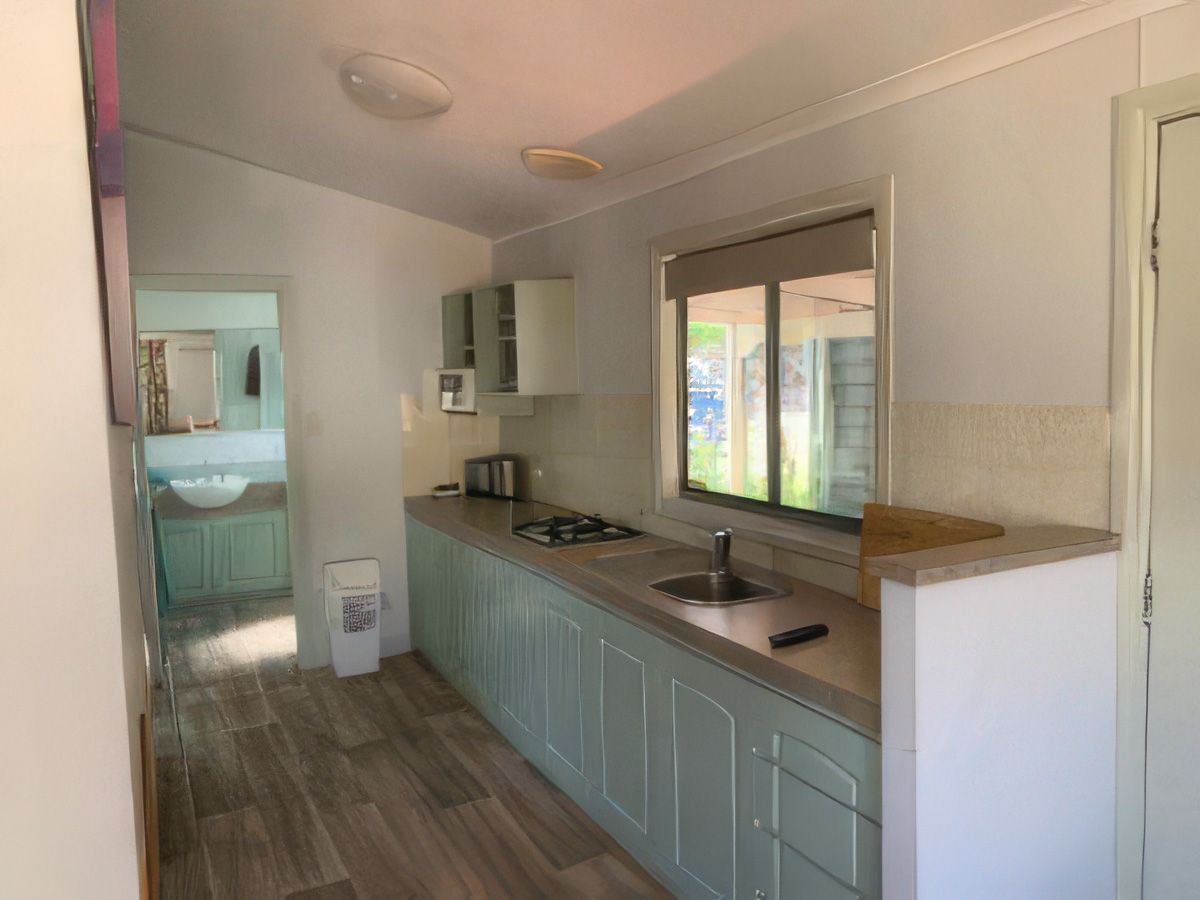 Narrow kitchen with light blue cabinets, white countertops, wood-look floor, and a window over the sink.