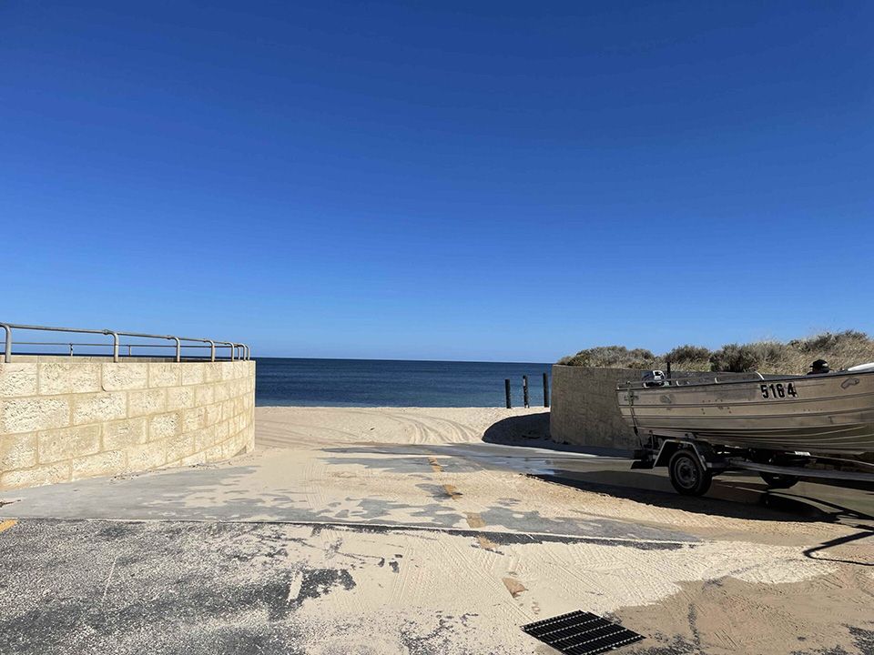 Sandy beach access ramp with parked boat trailer, overlooking calm blue ocean under clear sky
