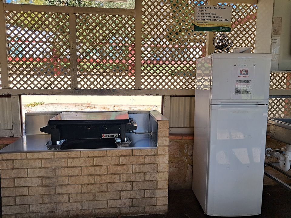 Outdoor patio with a brick barbecue grill and a white refrigerator under a shaded lattice wall