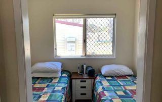 Small bedroom with two twin beds, colorful quilts, and a window between them.