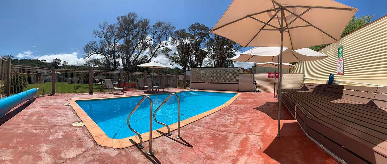 Backyard pool with red patio, beige umbrellas, and lounge chairs on a sunny day