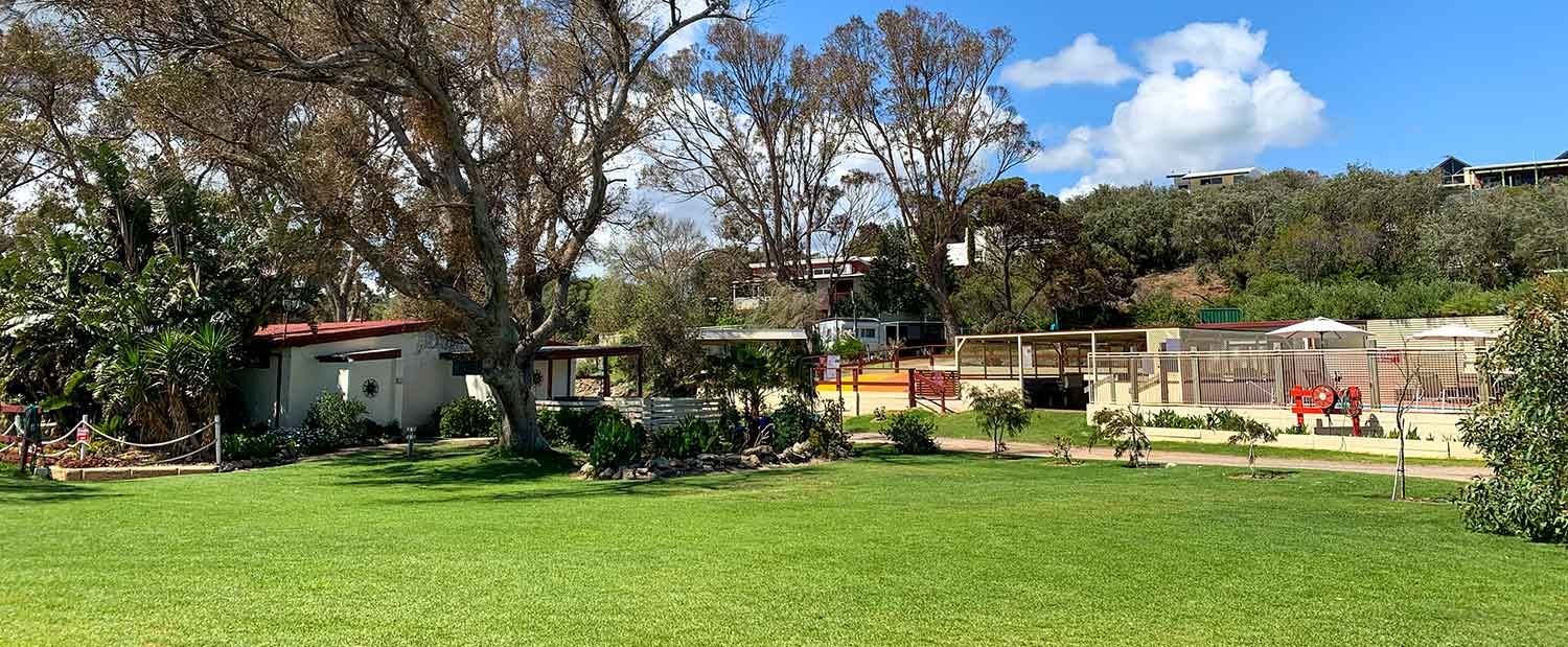 Wide grassy backyard with trees, a patio, and a red chair under a blue sky