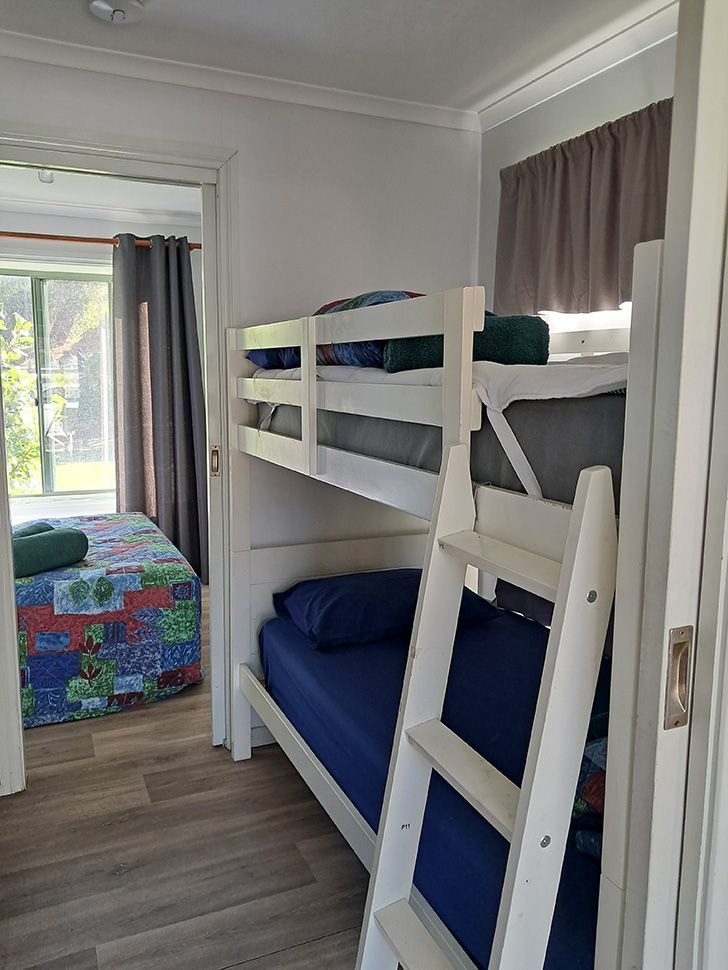 Small bedroom with white bunk beds, blue bedding, and a colorful quilt on the far bed.