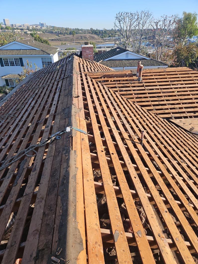Rooftop with weathered clay tiles and wooden battens overlooking a suburban neighborhood on a clear day