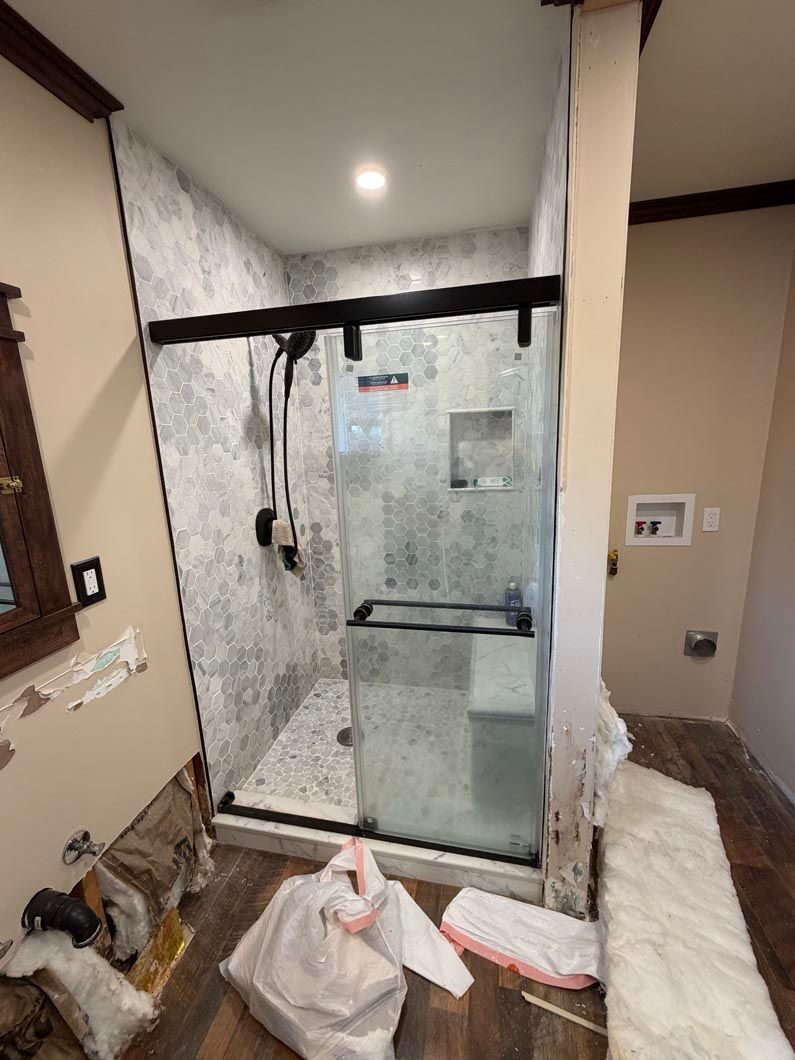 Bathroom with a glass shower enclosure, marble walls, and towels on the floor, under construction.