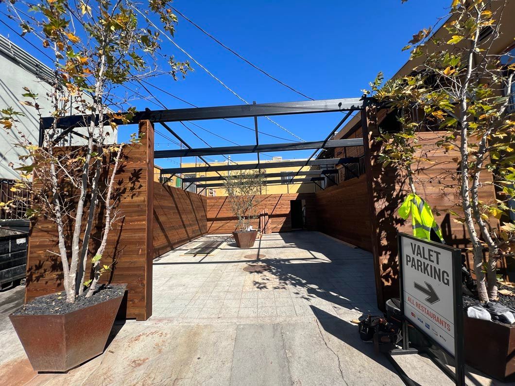 Outdoor patio under construction with brick walls, metal beams, and a sign at the entrance.
