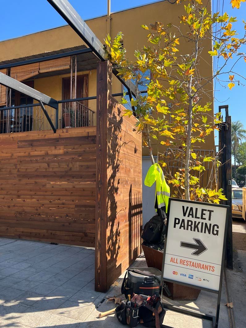 Valet parking sign beside a wooden building with yellow autumn leaves and a blue awning.