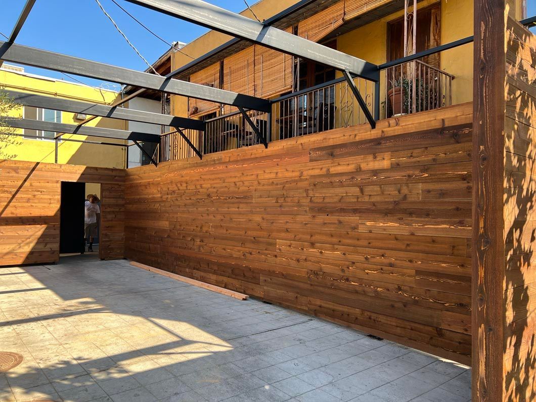 Wooden outdoor courtyard with black railings, stairs, and a bright blue sky overhead.