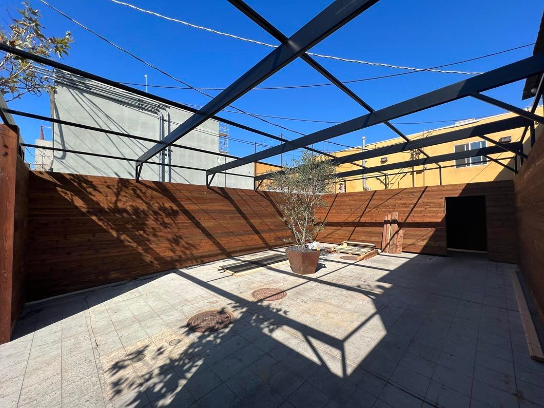 Empty brick-walled courtyard with tiled floor, open metal trellis, and a small tree in the center.