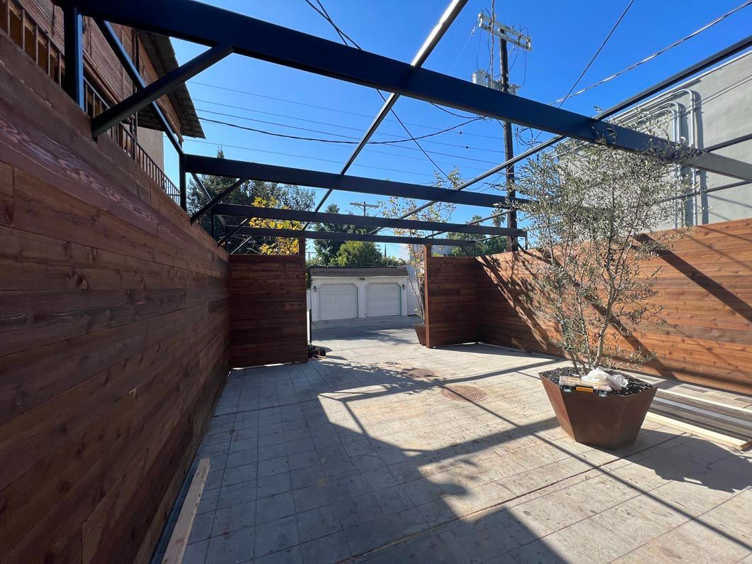 Wooden patio with pergola beams, brick walls, potted plant, and bright blue sky above.