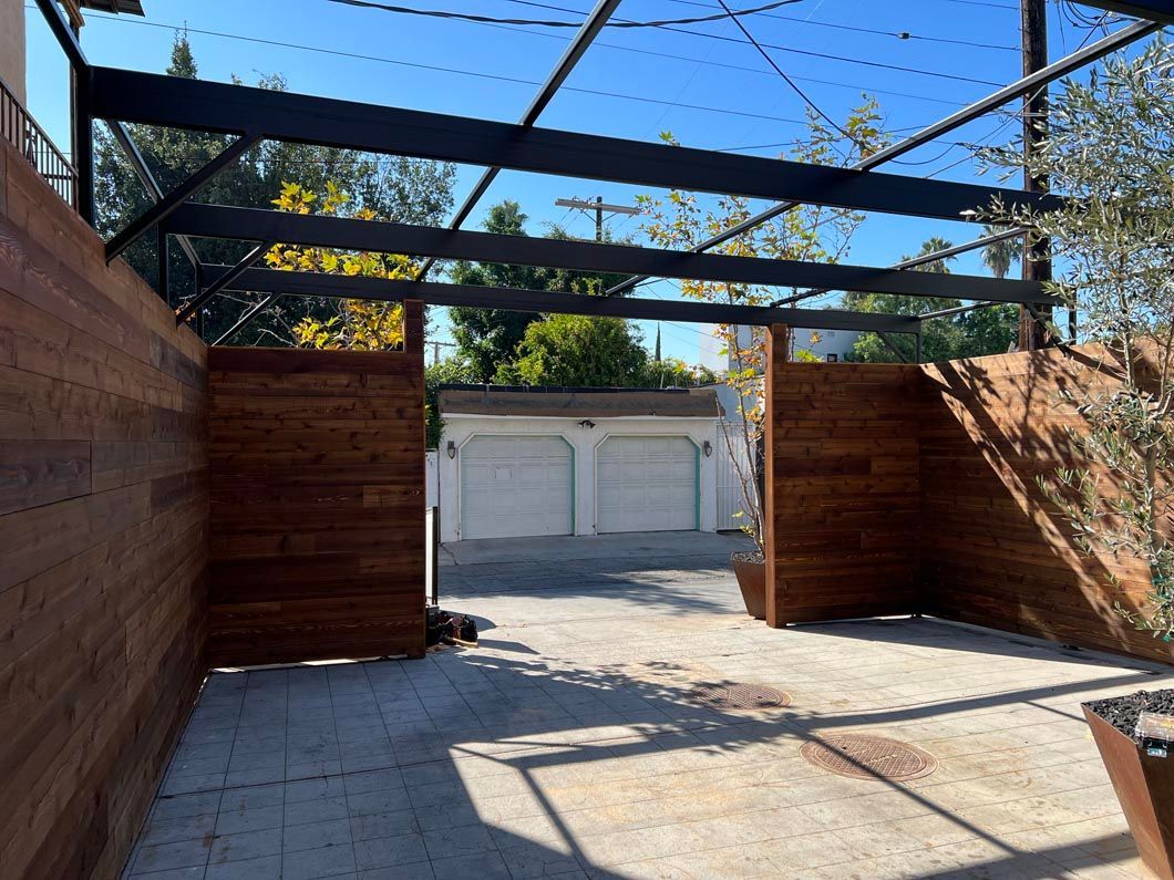 Wooden patio walkway with overhead beams, leading to a white garage under clear blue sky.