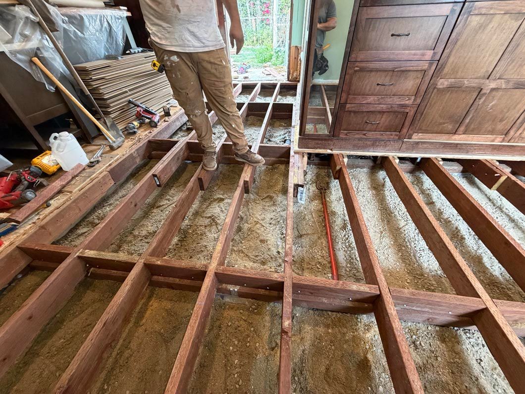 Person standing on exposed wooden floor joists inside a room under renovation