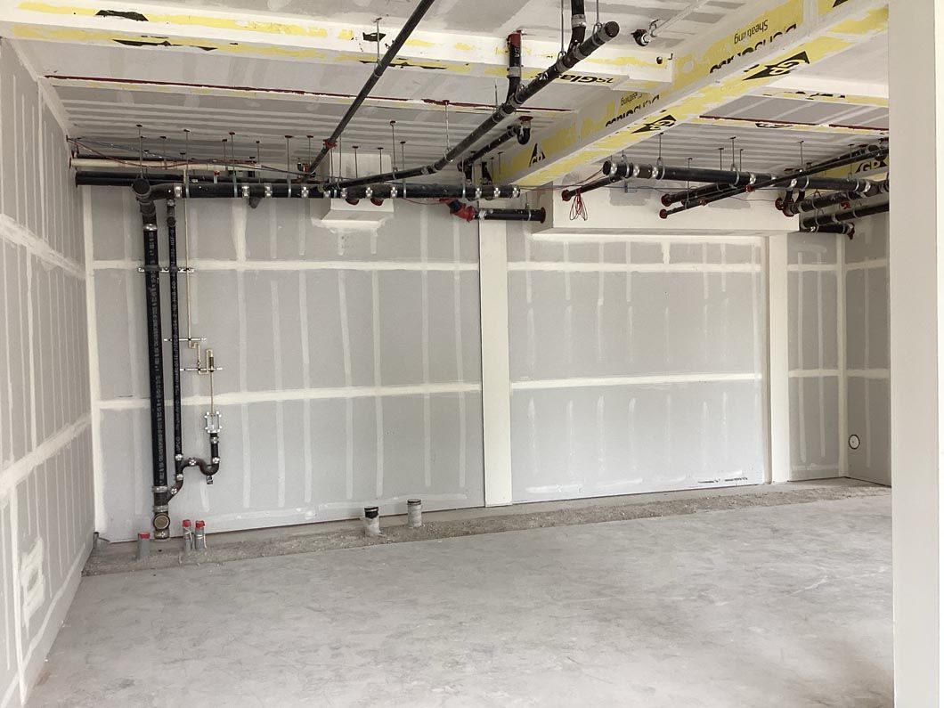 Empty unfinished room with exposed ceiling, drywall walls, and concrete floor under construction