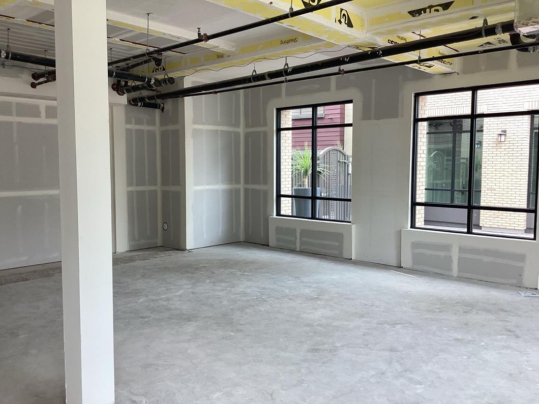 Empty unfinished room with exposed ceiling, white walls, and large windows with blinds.