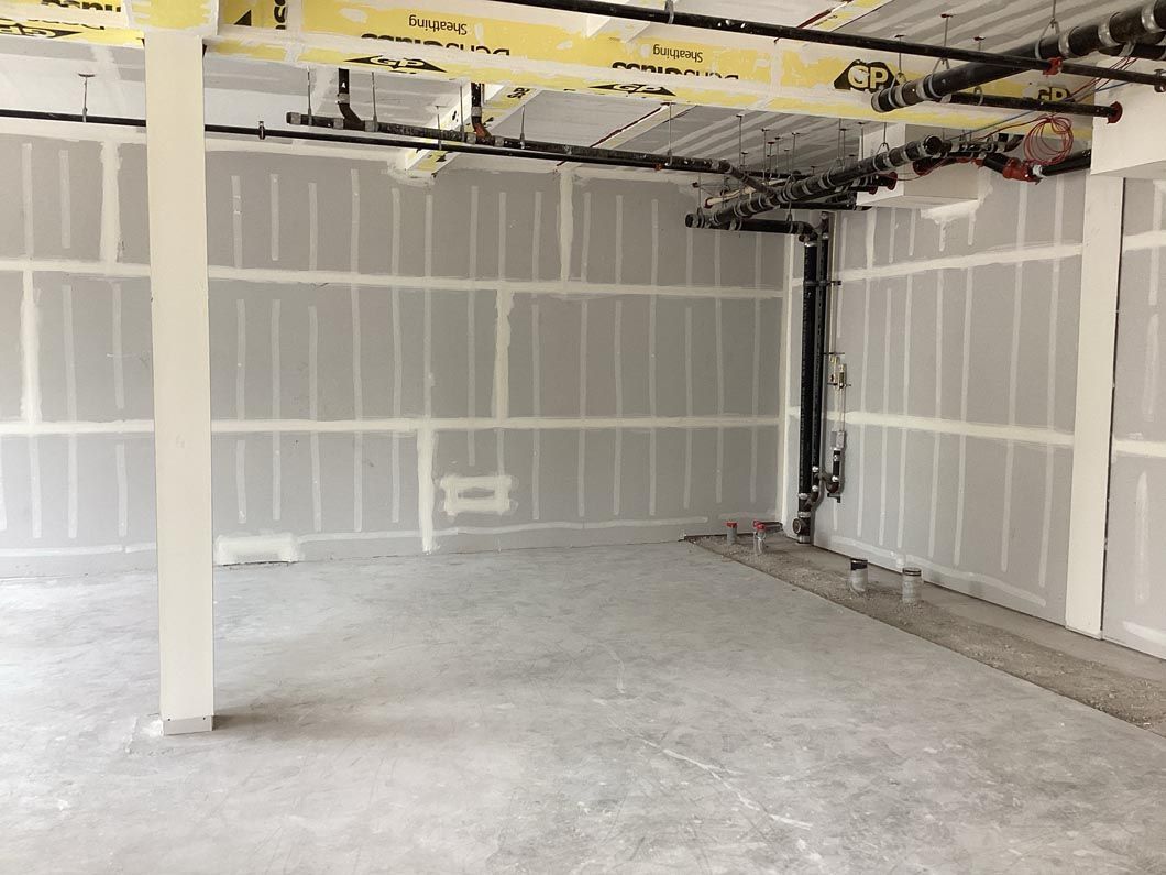 Unfinished garage interior with drywall, concrete floor, and exposed ceiling beams and pipes.