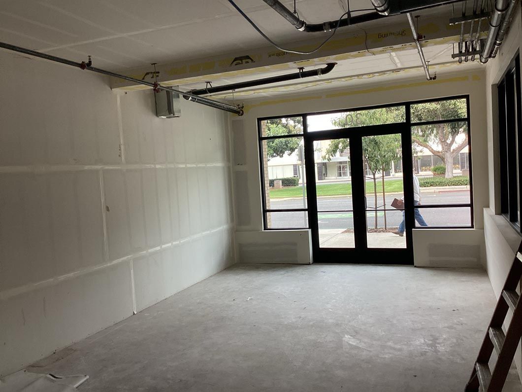 Empty storefront interior with white walls, concrete floor, and glass entrance doors at the front