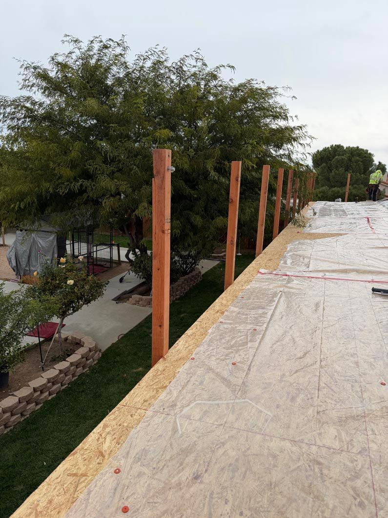 Partially constructed rooftop walkway with wooden posts and plastic covering beside trees