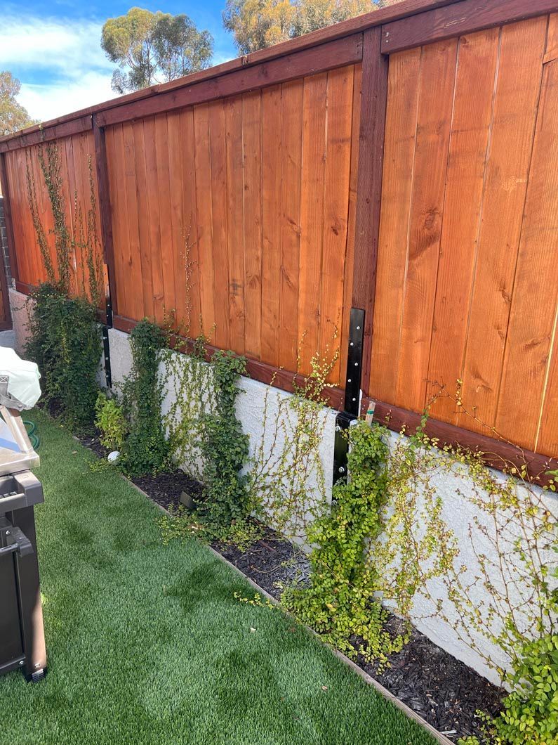Wooden fence with vertical slats beside a lawn and young shrubs along a white planter wall