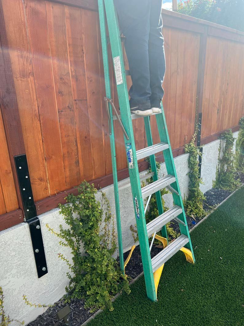 Person on green ladder working on wooden fence outdoors