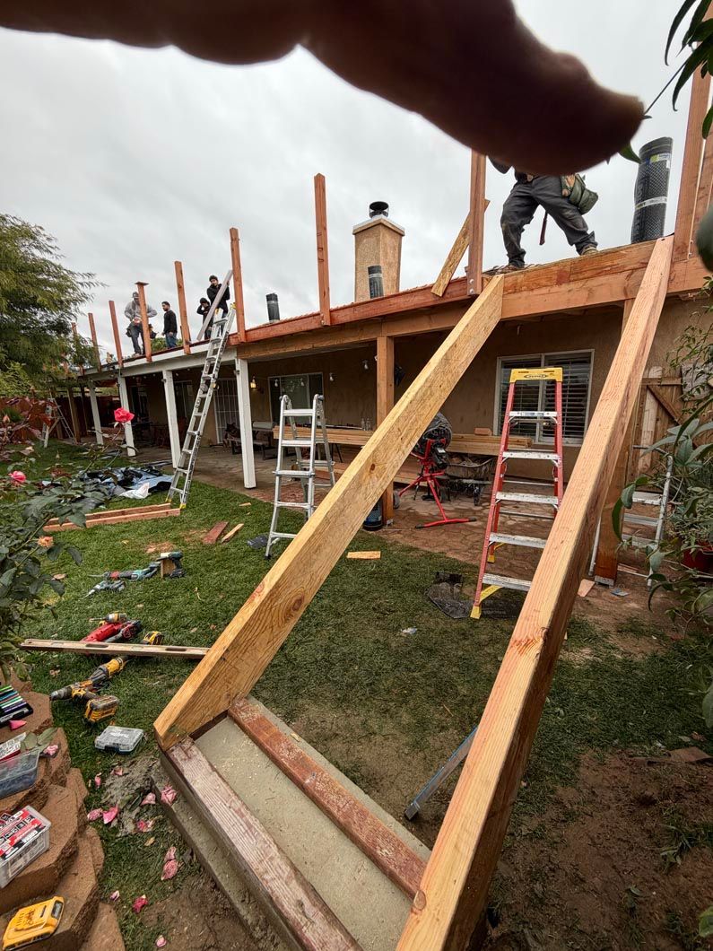 Wooden braces support a house under construction, with scaffolding and ladders in a yard.