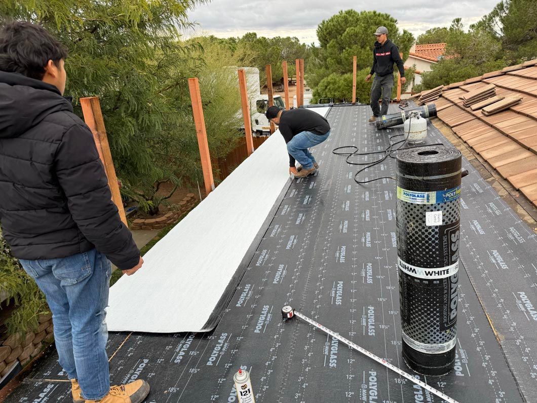 Workers installing roofing on a flat roof with black underlayment, white panels, and terracotta tiles nearby