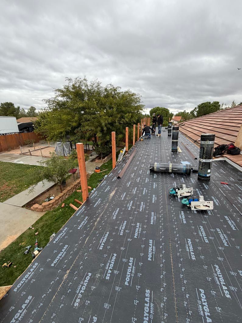 Roofer working on a flat roof under cloudy skies, with tools and materials laid out nearby.