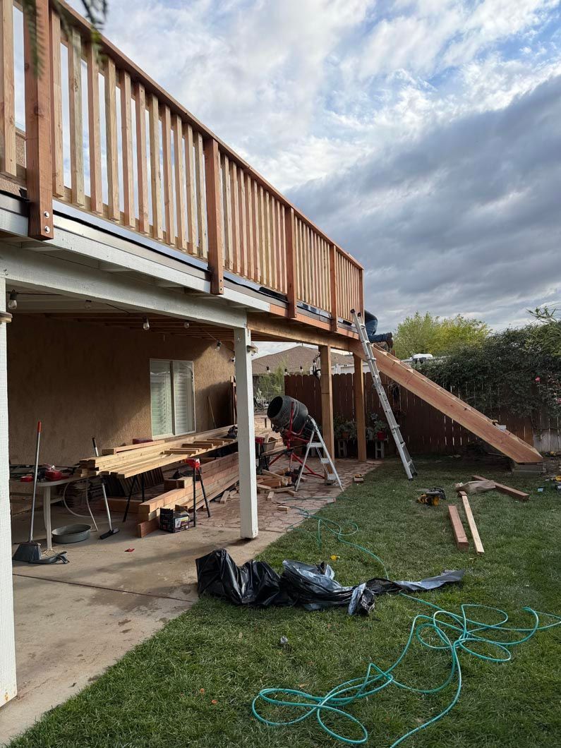 Backyard deck under repair, with tools, lumber, and a long stairway beside the house
