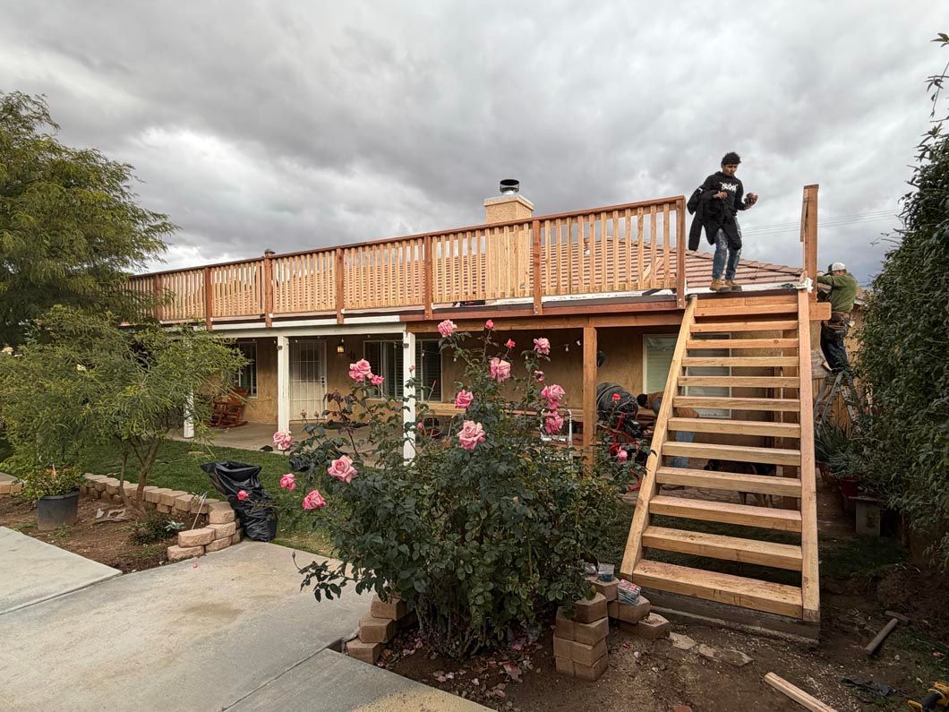 Man on wooden stairs beside a house with a raised deck and pink rose bushes in the yard