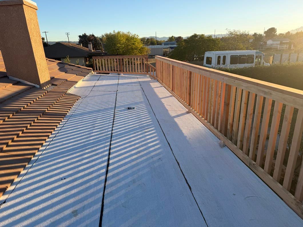 Sunlit rooftop deck with wooden railing and patterned shadows across the white floorboards.