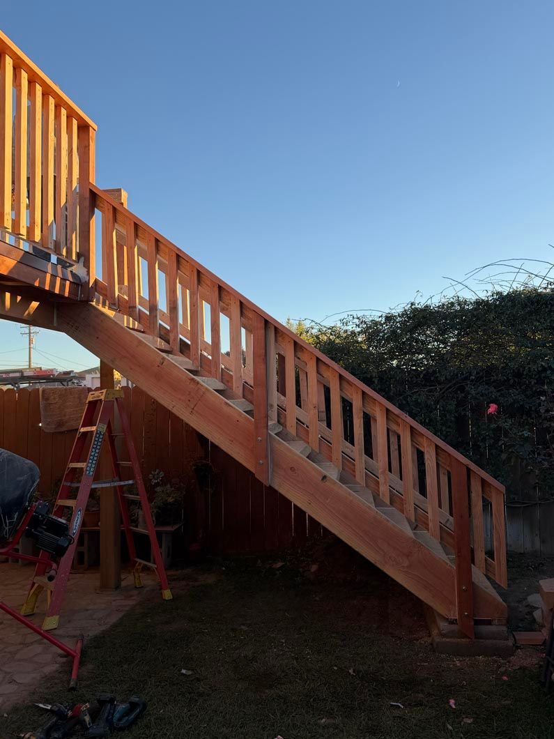 Wooden outdoor staircase and deck with orange railings beside a garden fence