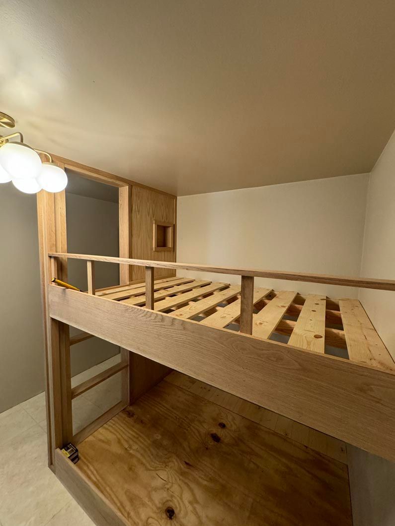 Wooden loft bed with open slats in a small room, viewed from below beside a staircase.