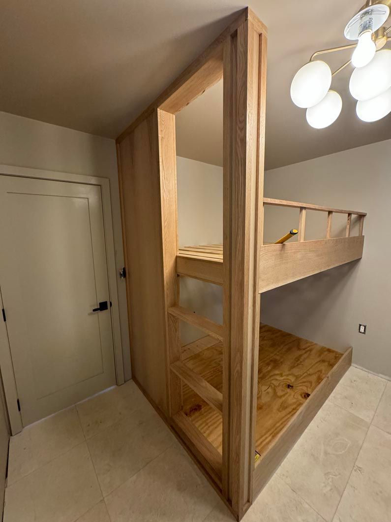 Loft-style bunk bed in a small room with wood frame and ladder beside a white door.