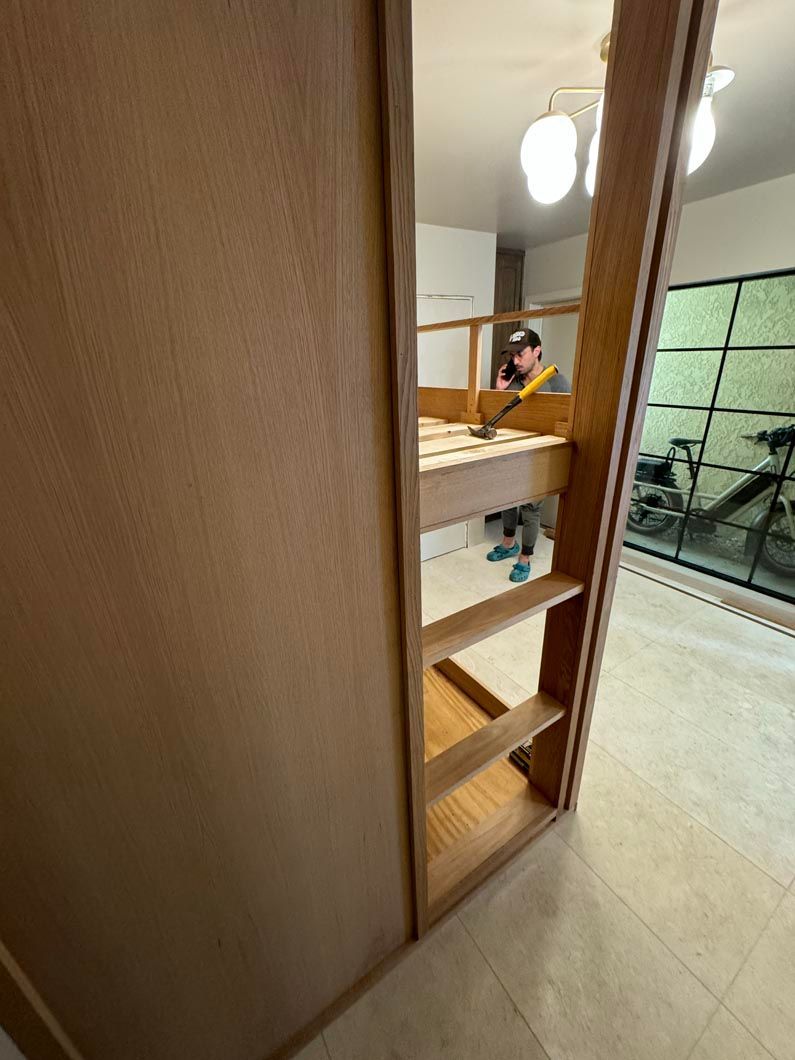 Wooden shelves beside a bed in a bright room, with a person seated in the background.