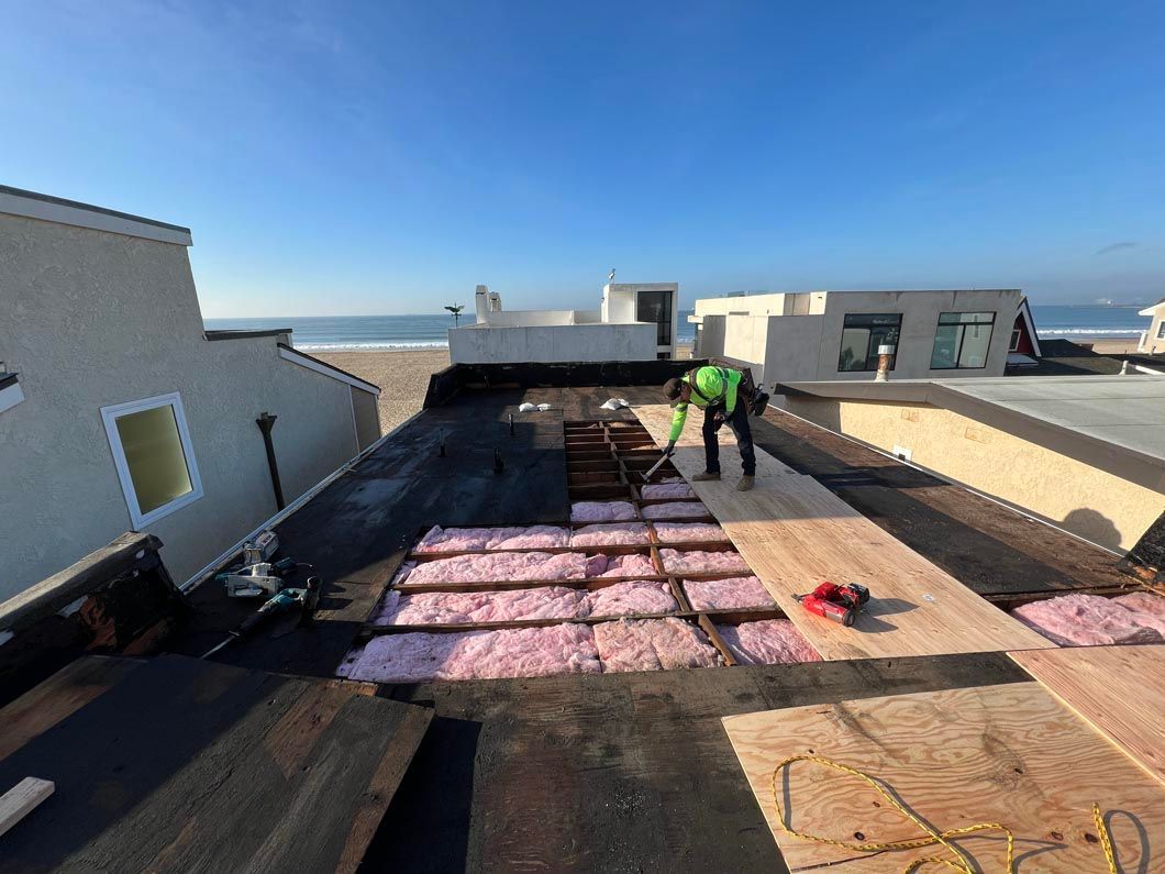 Roof under construction with workers, pink insulation panels, and ocean view under a clear blue sky