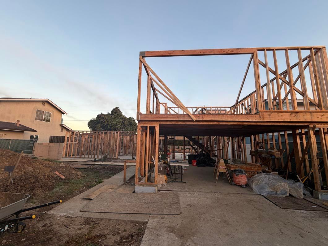 Partially built wooden house frame with an open garage on a dirt driveway at sunset