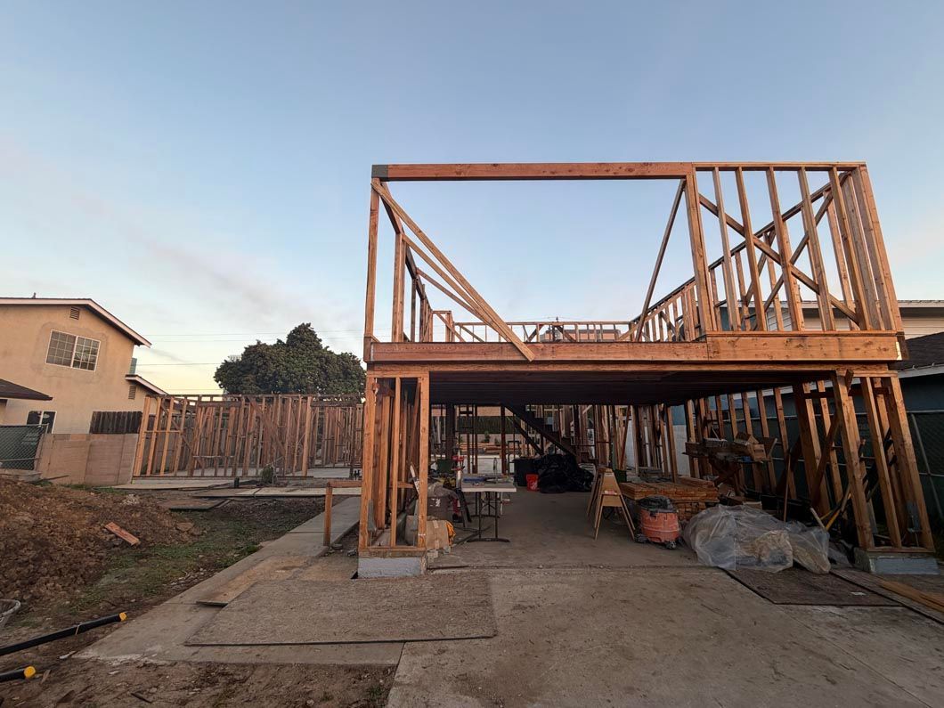 Unfinished two-story wooden house frame under construction on a bare lot at dusk