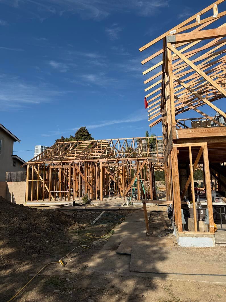 Partially framed house under construction on a sunny day, with wooden beams and a blue sky.