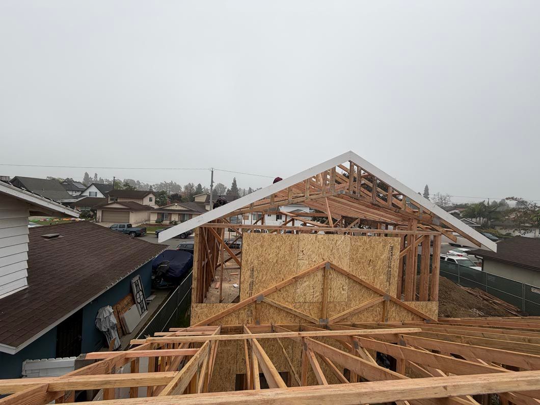 Wood-framed house under construction with roof trusses and neighboring homes in the background