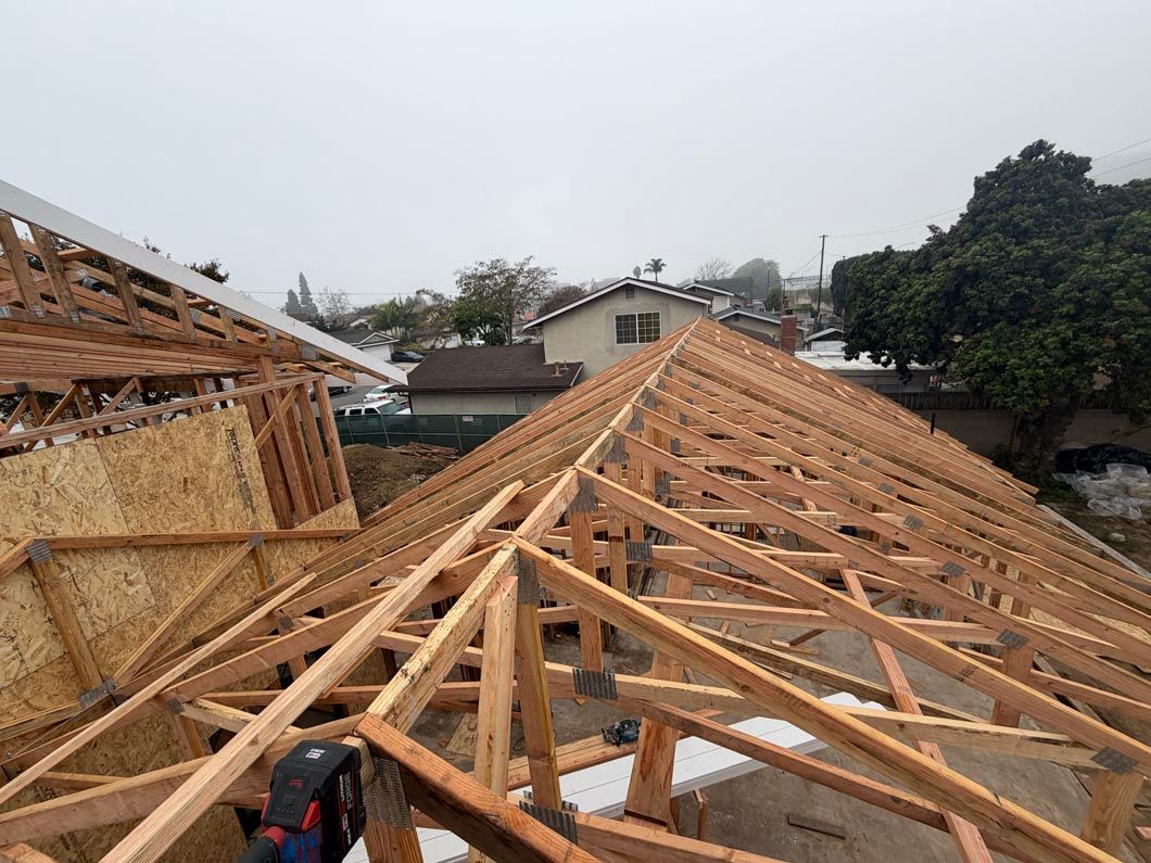 Wooden roof trusses under construction on a house site, with a cloudy sky and nearby trees.