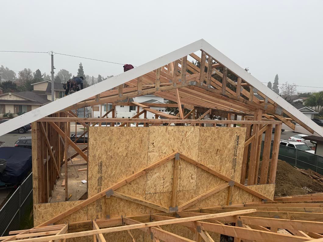 Partially built wooden house frame with exposed trusses and OSB sheathing on a cloudy day