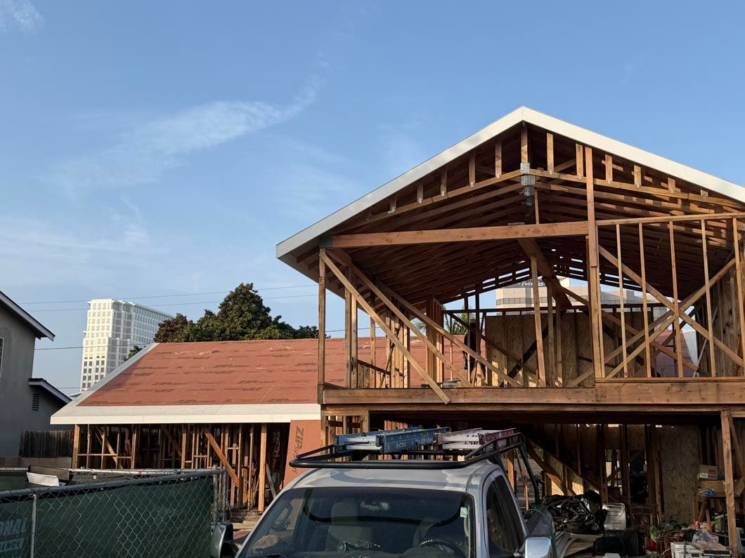 Partially built wooden house with exposed framing and a parked SUV in front under a blue sky