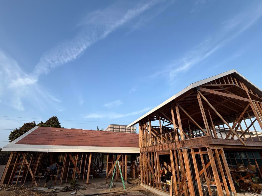 Wood-framed buildings under construction with a red roof and open sky