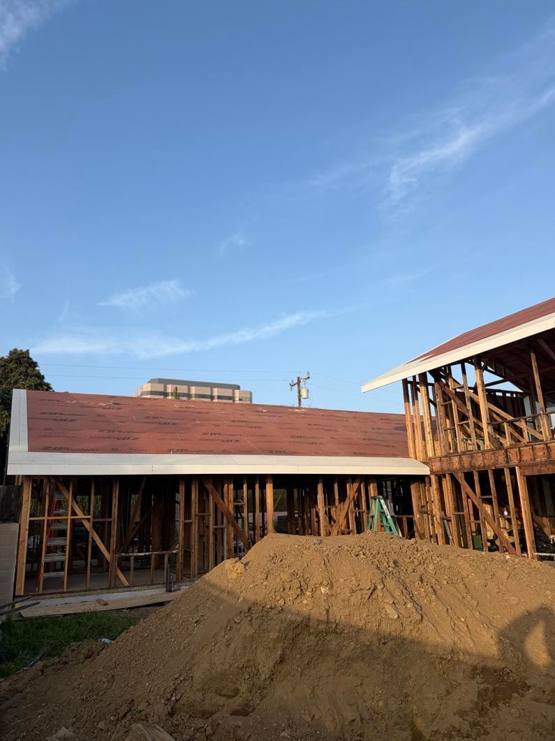 Partially built house with red roof, wooden scaffolding, and a dirt pile under a blue sky