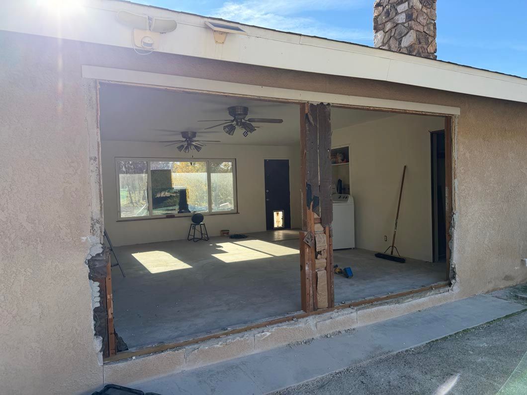 Open garage or patio area with exposed framing, concrete floor, ceiling fan, and unfinished walls.