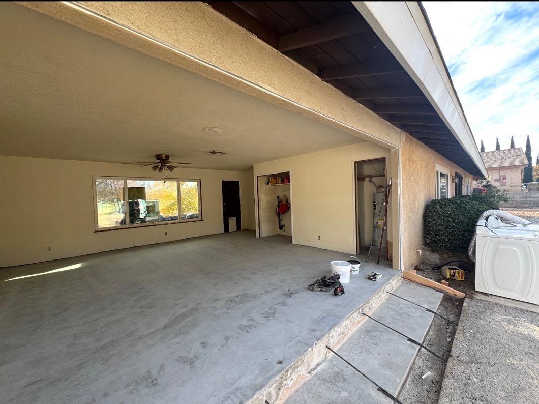 Covered driveway or patio with concrete floor, beige walls, and open garage-style space in daylight