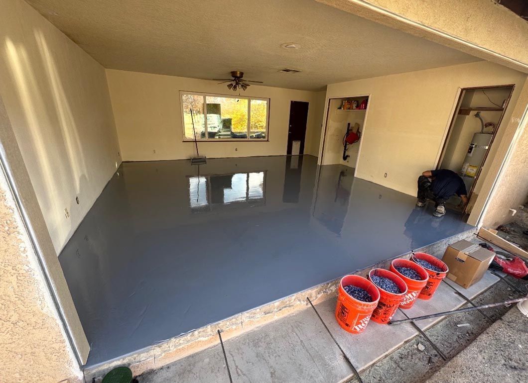 Empty room with glossy gray floor, large window, and red buckets near the entrance.