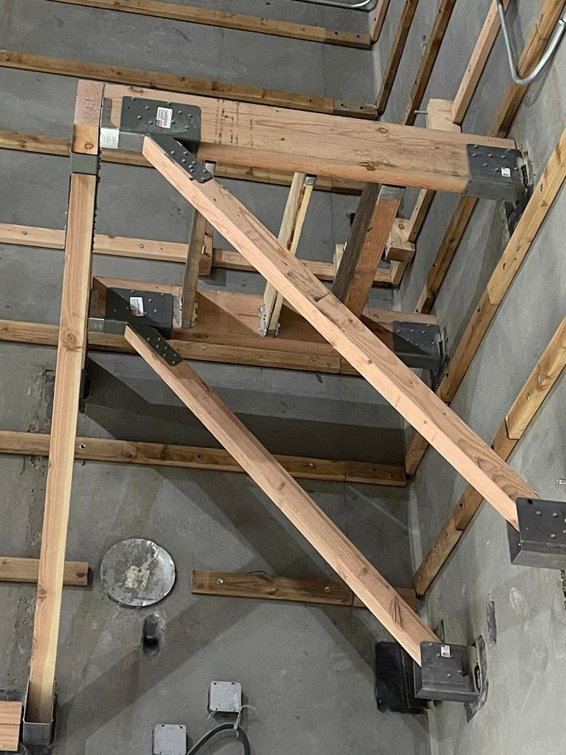 Wooden braces and a beam mounted to a ceiling frame in an unfinished room with a hanging light.