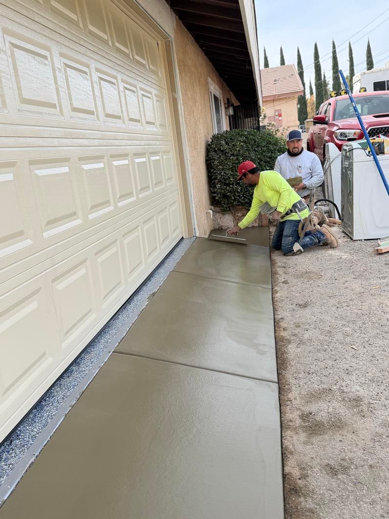 Workers smoothing fresh concrete along a garage driveway beside a beige house
